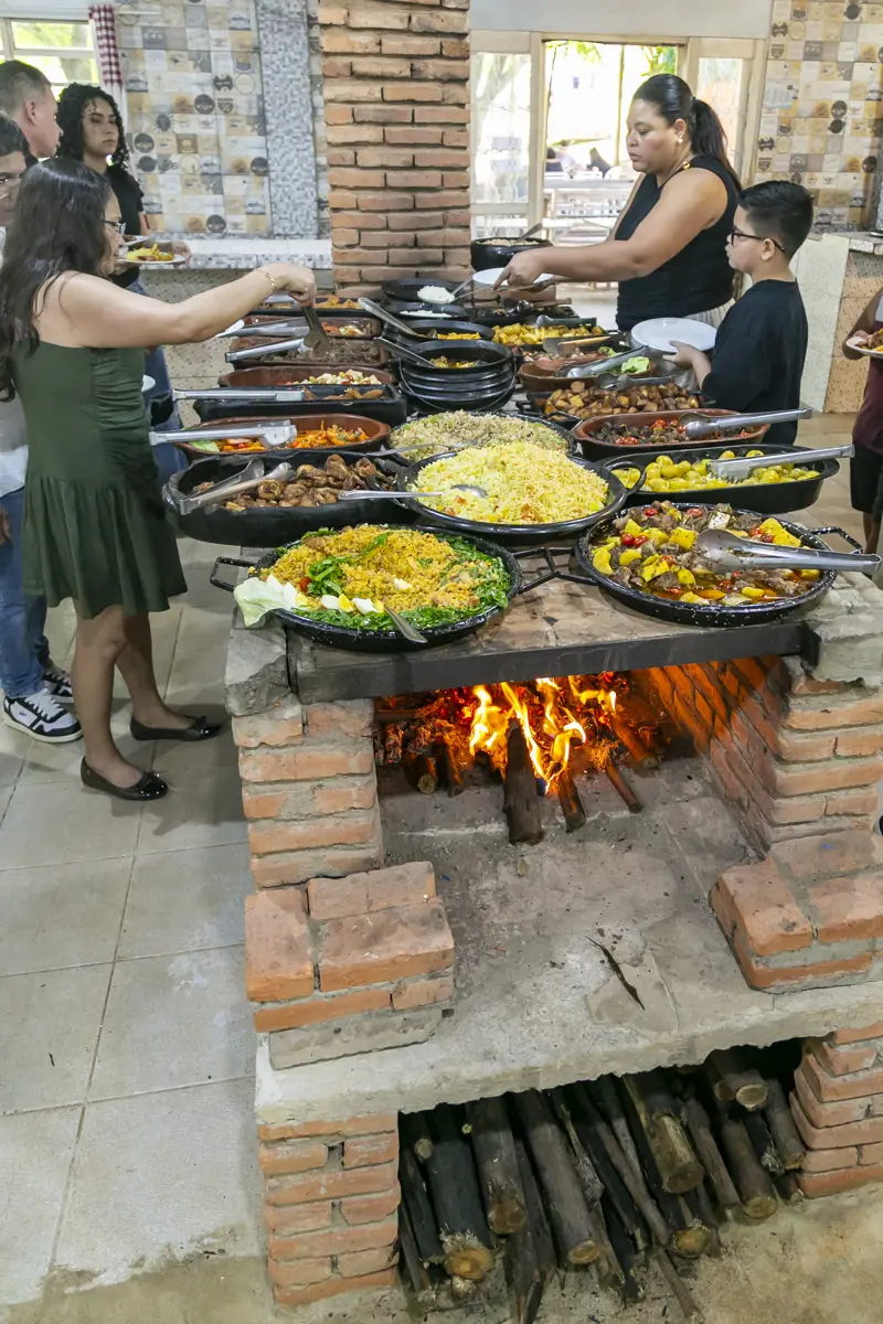 Clientes se servindo no buffet sobre o fogão a lenha aceso